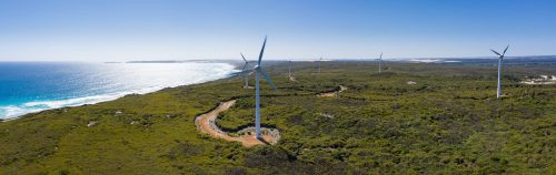 Panoramic aerial view of a coastal wind farm with multiple turbines along the lush landscape, highlighting renewable energy and natural scenery.