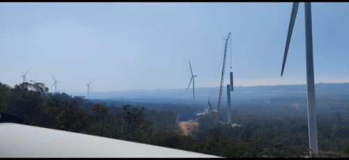 Panoramic view of wind turbine construction in a forested landscape, with a crane in the distance against a hazy sky, signifying green energy advancements.