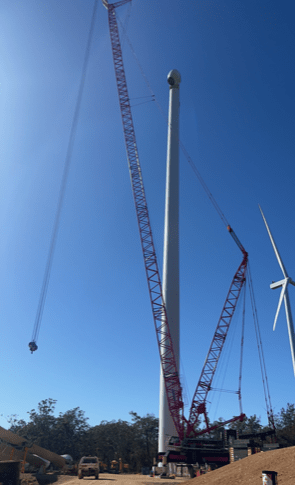 Tall red crane lifting a wind turbine tower against a bright blue sky on a wind farm, illustrating renewable energy construction and engineering.