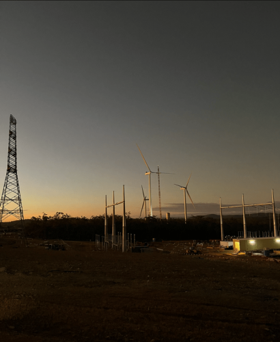 Dusk at a wind farm construction site with incomplete wind turbines and electrical structures, under a gradient sky transitioning from yellow to deep blue.