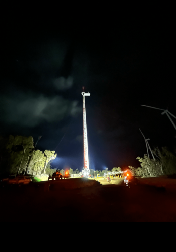 Illuminated wind turbine tower at night with spotlight beams cutting through the dark sky, reflecting the active work on sustainable energy projects