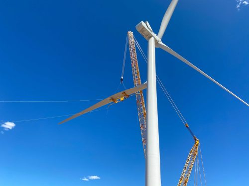 Installation of wind turbine blades using cranes against a vivid blue sky, showcasing the maintenance and setup of clean energy technology.