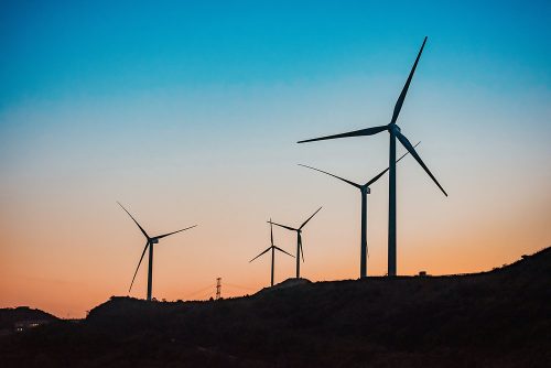 Wind turbines on a hill at sunset with a gradient sky transitioning from orange to blue, symbolising sustainable energy and eco-friendly power generation